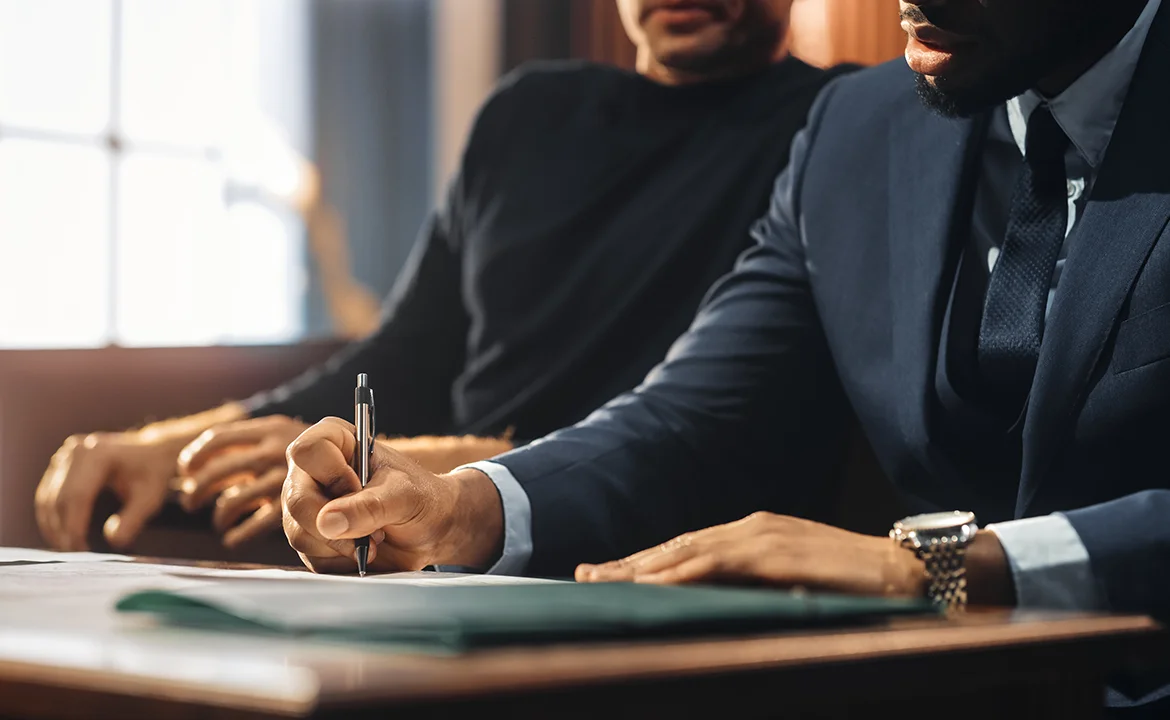 A lawyer diligently takes notes in the courtroom while sitting alongside their client.