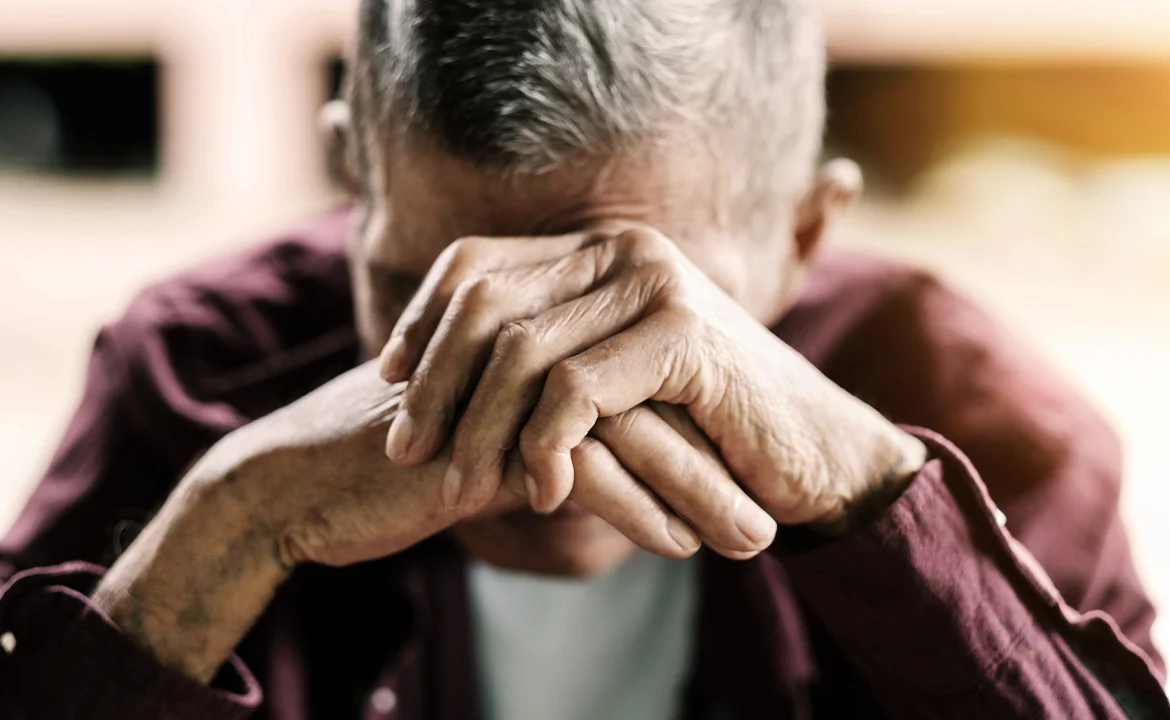 An elderly man with his hands covering his face