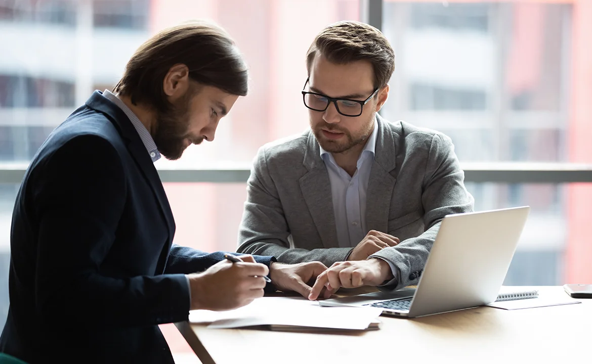 One man is pointing at a piece of paper while another man is attentively looking at it.